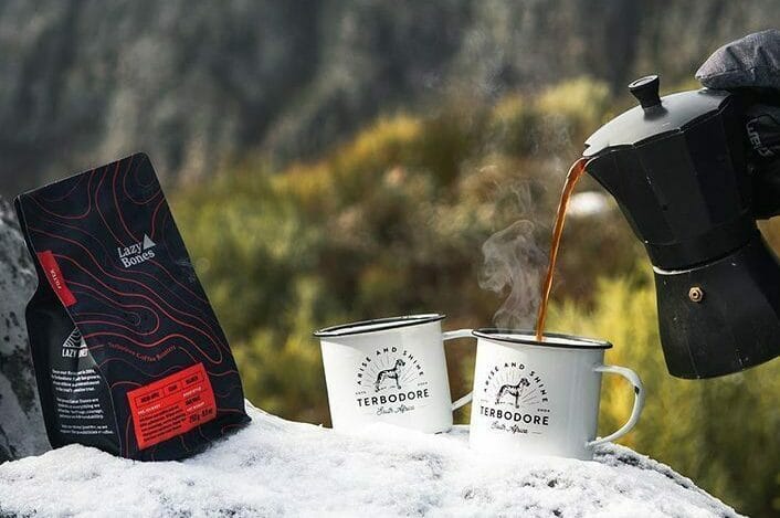 Coffee being poured into a Terbodore Travel mug resting on rocks covered in snow, Lazy Bones Coffee bag - Terbodore